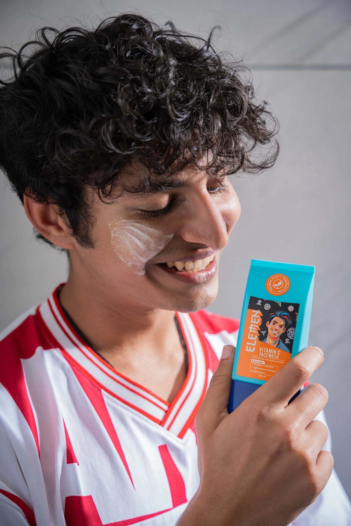 Boy holding a vitamin c facewash product with a visible brand logo against a neutral background